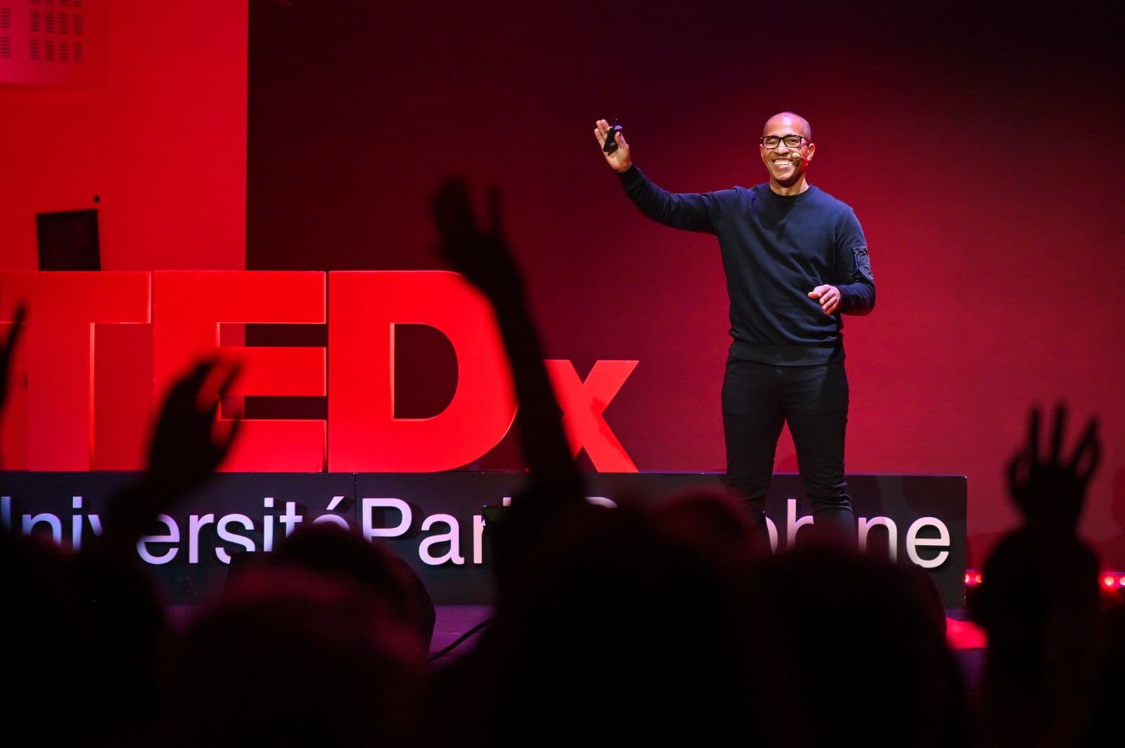 Salime Nassur on stage at TEDx Université Paris Dauphine, raising his hand towards the audience